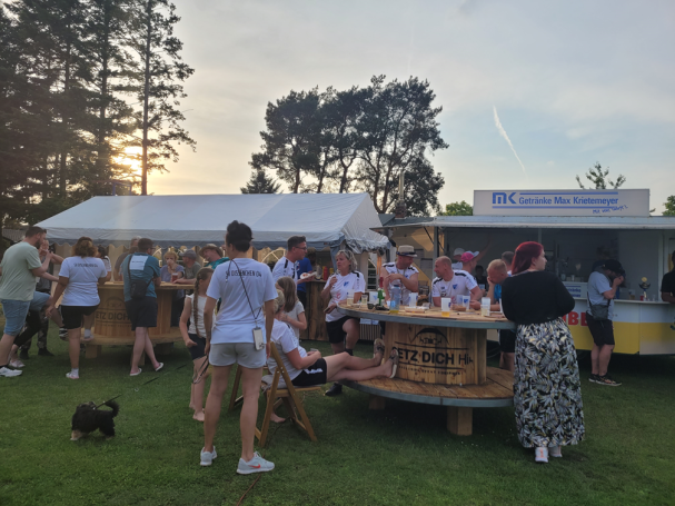 Menschen genießen Getränke an einem festlichen Stand im Freien bei Sonnenuntergang.