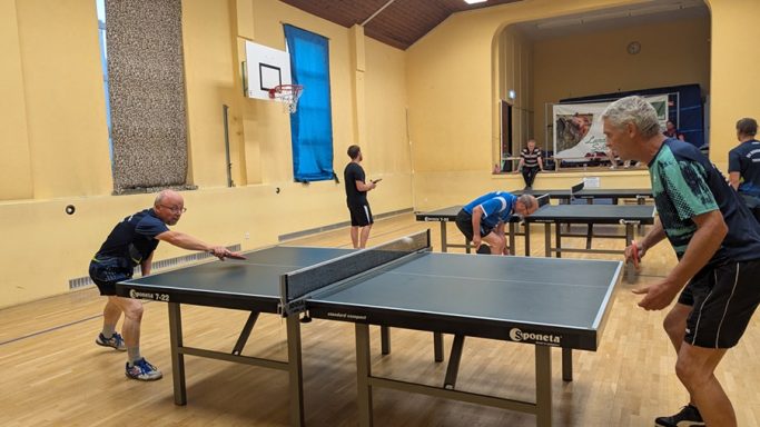 Voller persönlicher Einsatz Tischtennisspieler in einer Halle, mehrere Spieler an Tischen in Aktion.