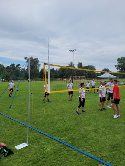 Jugendliche spielen Volleyball auf einem Sportplatz unter bewölktem Himmel.