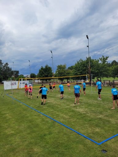 Das Finale Gruppe von Menschen spielt Volleyball auf einer Wiese unter bewölktem Himmel.